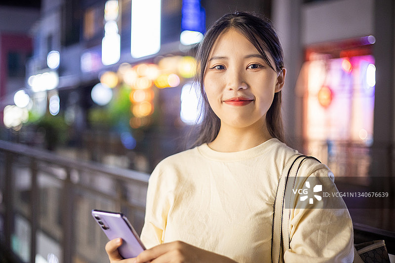 年轻的亚洲女人在夜街拍照图片素材