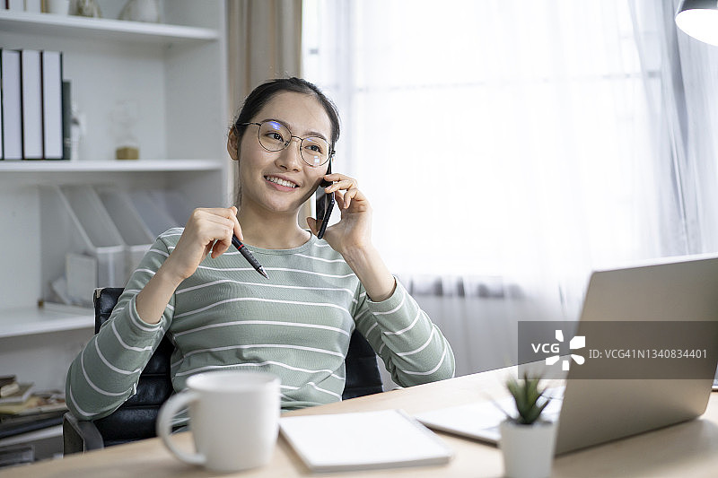 微笑的女性自由职业者在电话中，坐在家里的笔记本电脑图片素材
