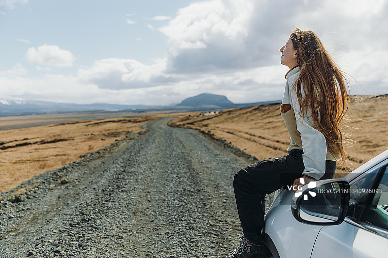 在冰岛的公路旅行中，一名年轻女子坐在车里，凝视着美丽的山景图片素材