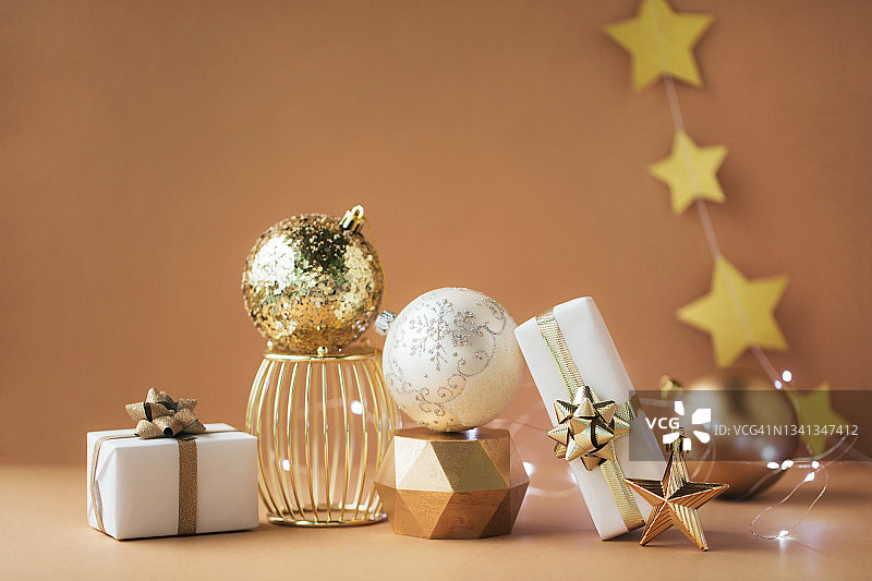圣诞构图由两件白色礼物，金色的星星，金色的讲台上三个不同的球和米色背景上的花环组成。新年概念图片素材