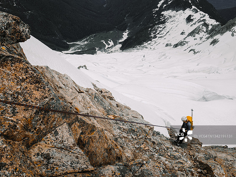 登山者从高出引人注目的冰川的岩壁上攀爬而下图片素材