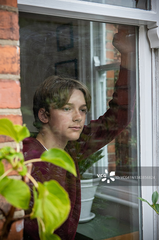 一个十几岁的男孩看着窗外图片素材