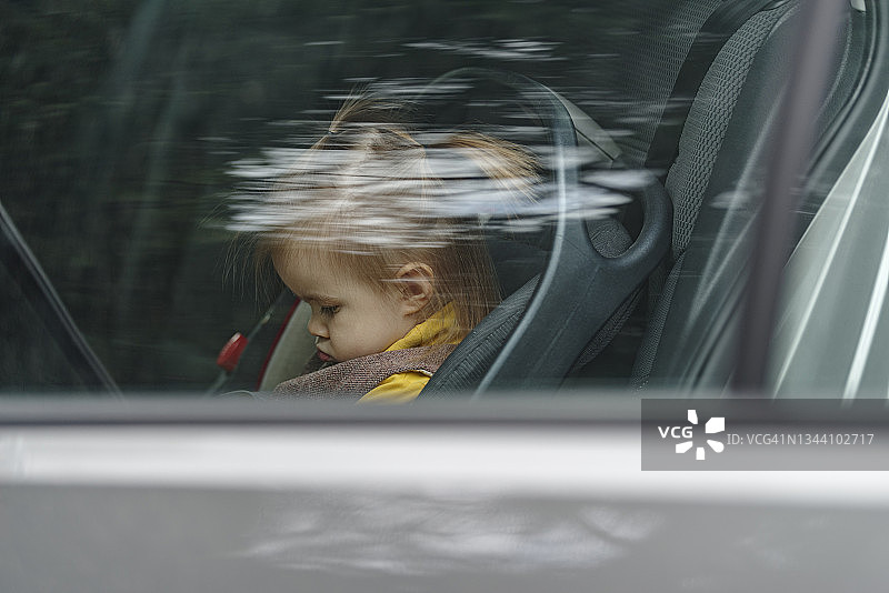 小女孩被绑在汽车座椅上。透过窗户看图片素材