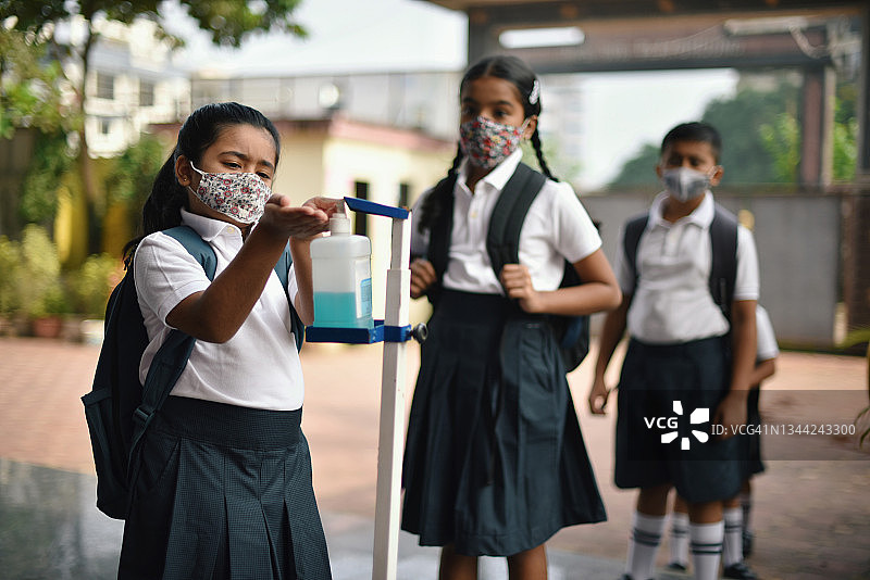 学生们戴着防护口罩，在学校门口排队，使用消毒剂图片素材