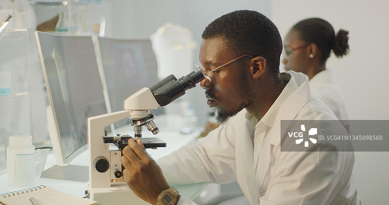 非洲种族科学家与显微镜。背景电脑屏幕图片素材