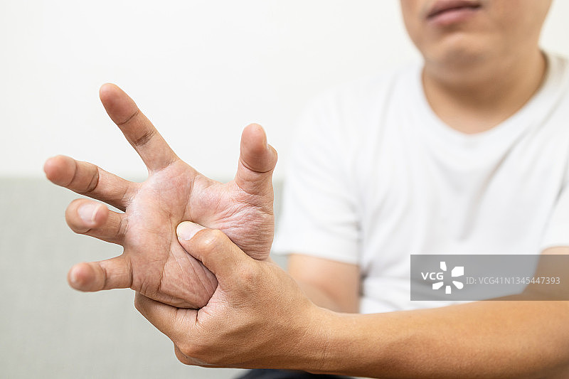 亚洲中年男性患者患有手部麻木疼痛，关节炎，肌腱问题引起手指抽搐，触发手指疾病，关节僵硬，按摩他的手掌，保健概念图片素材