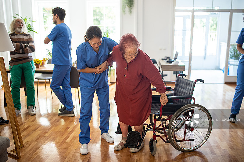 护理员协助老年妇女从轮椅上站起来图片素材