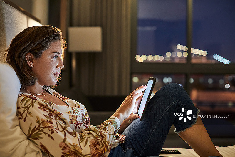 一名女子在酒店房间的床上使用电子平板电脑图片素材