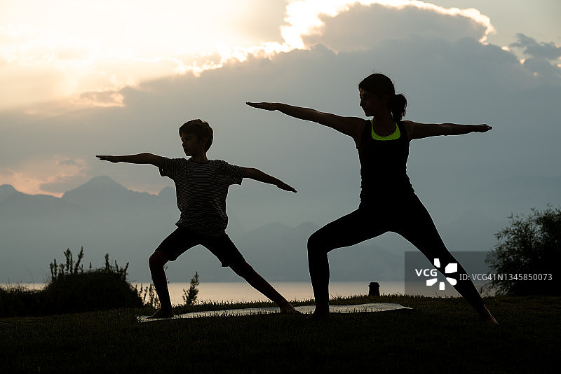 日落时分，一名成年女子和一名8岁男孩在做瑜伽图片素材
