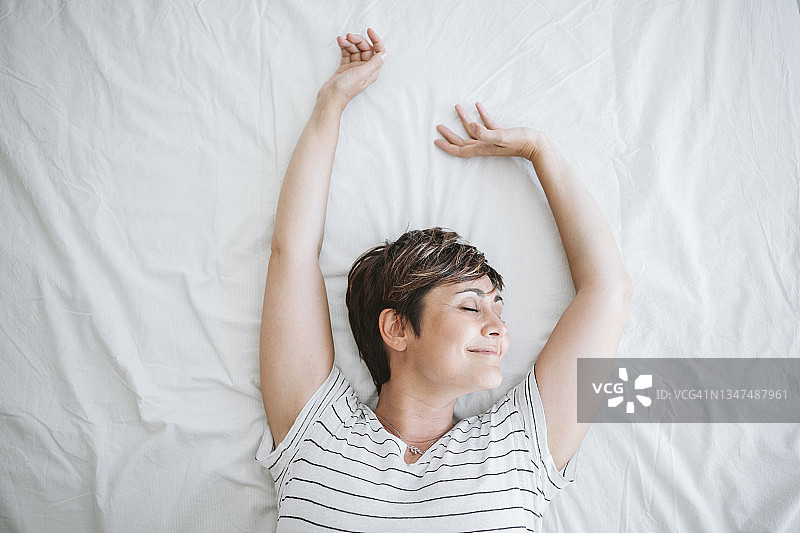 微笑的女人举起双臂躺在家里的床上图片素材
