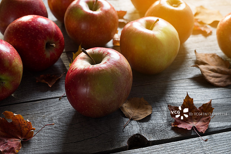 红色的苹果和落在木头背景上的桦树、枫树和白杨的黄叶。水果在厨房的桌子上。有机农产品的种植。素食、纯素、生食和饮食的概念。秋天的自然背景。收割。图片素材