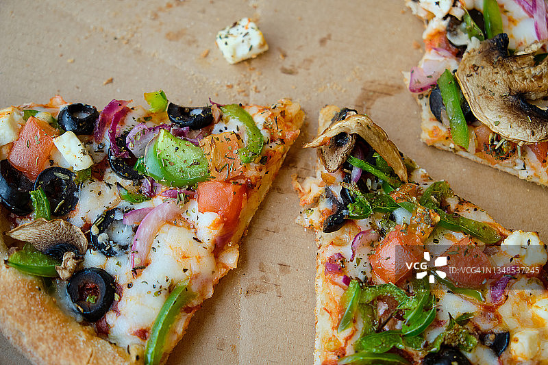 在咖啡馆或披萨店的木桌上，有硬纸盒或包装的意大利蔬菜披萨片，奶酪和蘑菇。素食。快餐。图片素材