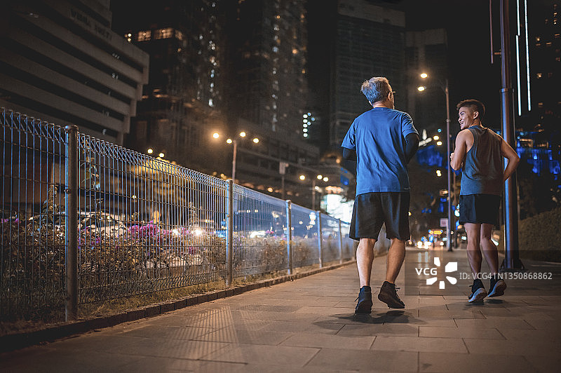 后视镜一名亚裔中国男子鼓励他的父亲晚上下班后一起在城市里慢跑图片素材