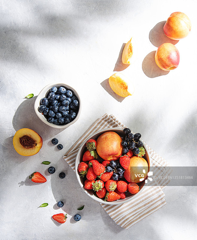 新鲜的有机夏季浆果和水果草莓，蓝莓，桃子和葡萄在一个白色的盘子上与晨光阴影的浅色背景。俯视图和复制空间图片素材