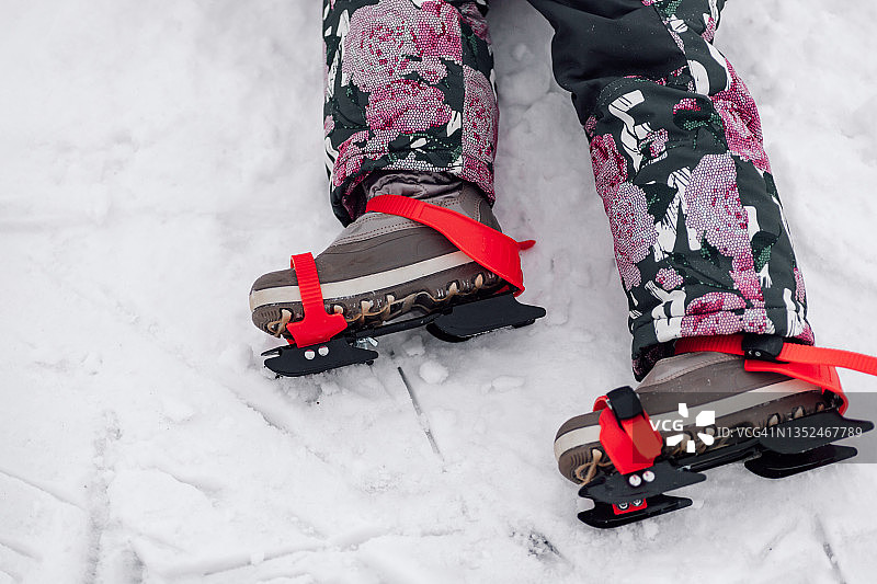 孩子溜冰鞋。儿童冰鞋与冬季靴子与红丝带的特写，侧视，雪的背景图片素材
