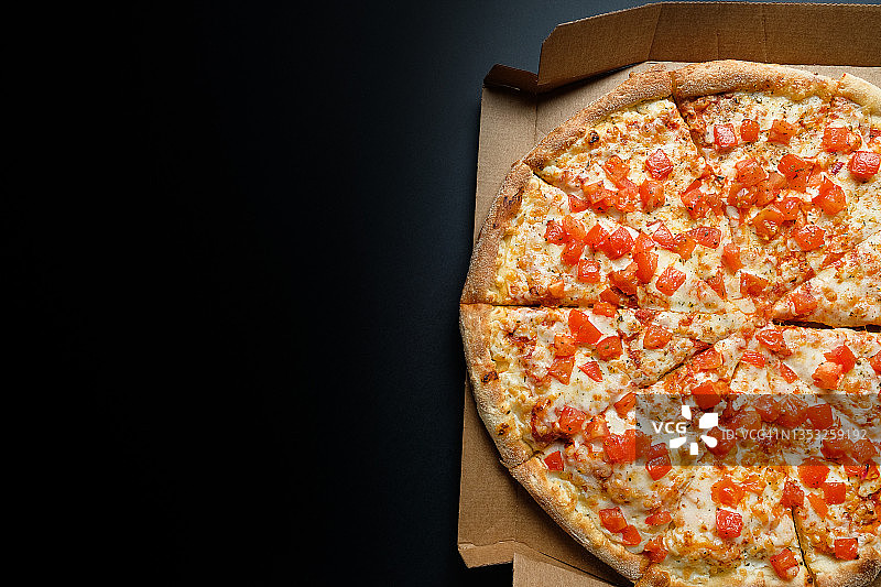 装在披萨盒里的意大利披萨，外卖时放在黑色背景或桌子上。玛格丽塔比萨配番茄和奶酪，切片，不含肉。素食的概念，快餐垃圾食品。送货到家或上班。复制的空间。图片素材