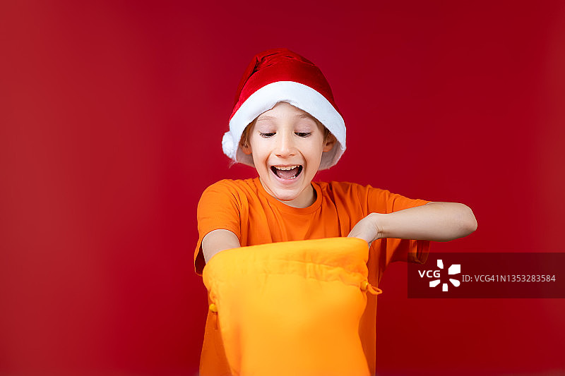 一个在红色圣诞背景上戴圣诞帽的男孩图片素材