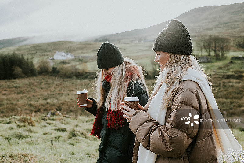 秋天，两个金发女人拿着外带的咖啡杯走在乡间。图片素材