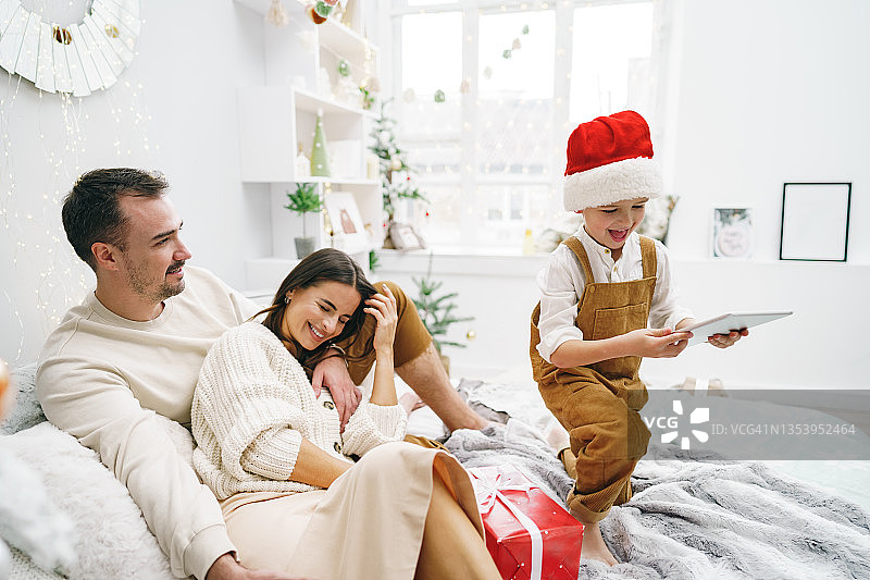 圣诞节，幸福的家庭在床上玩电子平板电脑图片素材