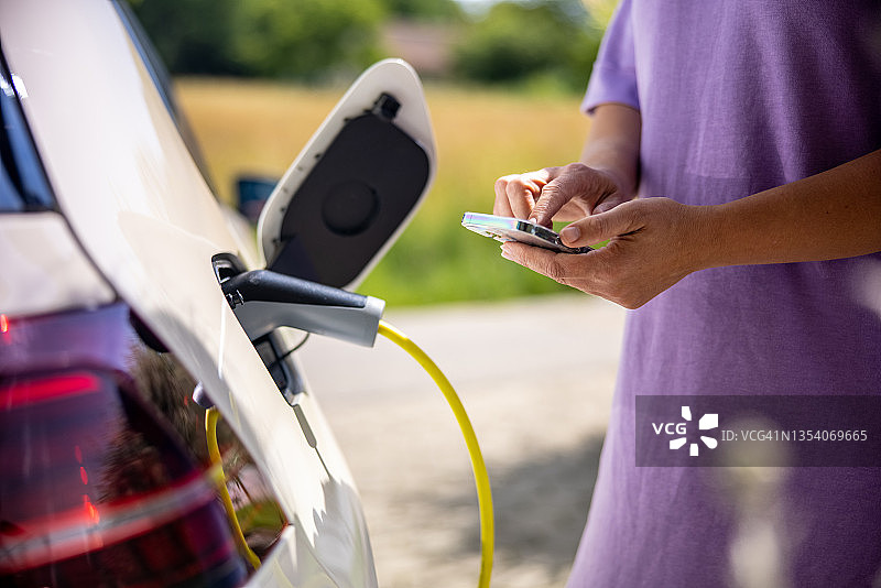 一名妇女一边用手机一边给电动汽车充电图片素材
