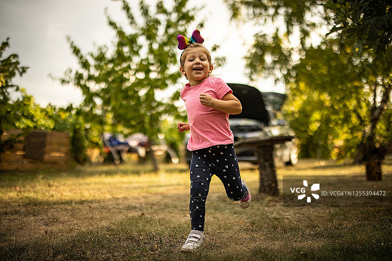 可爱的微笑的女孩在后院的草地上跑步图片素材