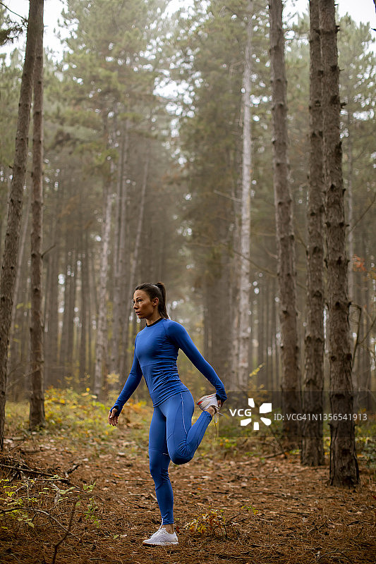 穿着蓝色运动服的年轻女子在秋天的森林里伸展运动图片素材