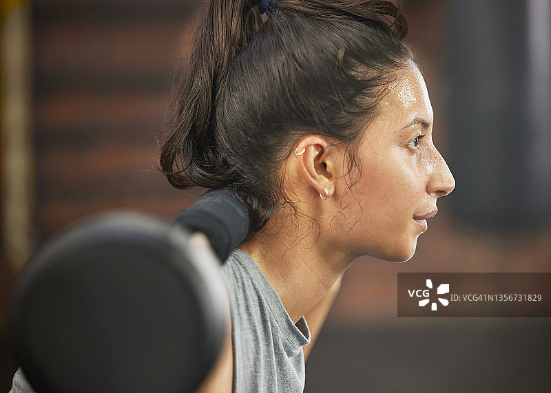 一个运动的年轻女子在健身房拿着杠铃锻炼图片素材