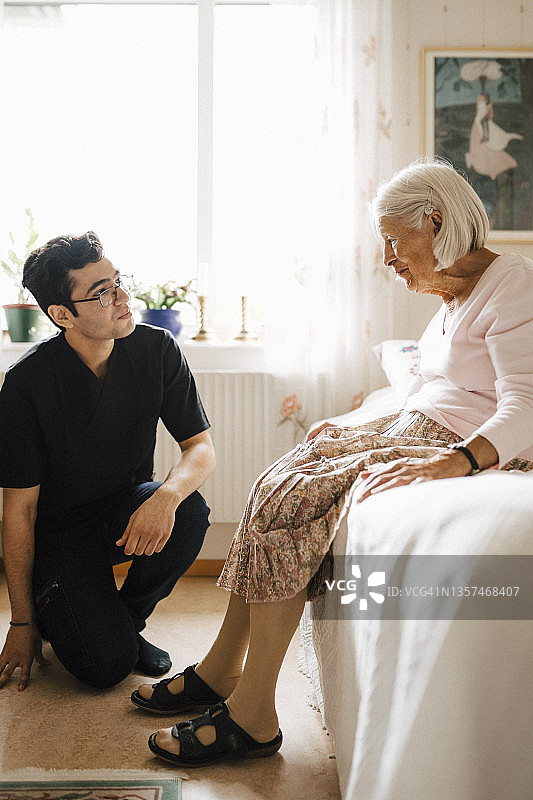 一位老年妇女在家中的卧室里与年轻的男性保健工作者交谈图片素材