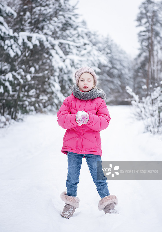 一个穿着鲜艳夹克的小女孩在冬天的森林里玩耍图片素材