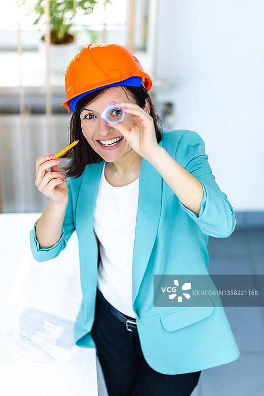 积极的女工程师的照片，戴着橙色的头盔，透过卷纸。图片素材