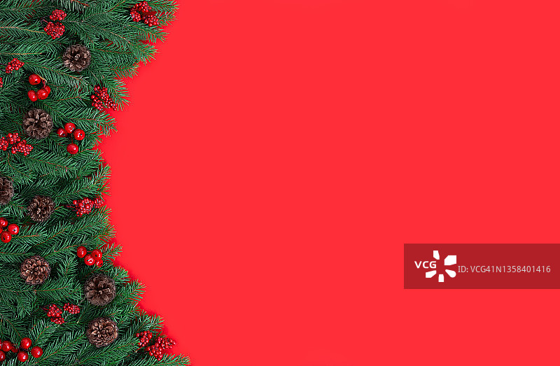 圣诞节边界与冷杉树枝，球果和浆果在一个红色的背景。圣诞红的背景。新年。贺卡。复制空间，顶视图，平铺。图片素材