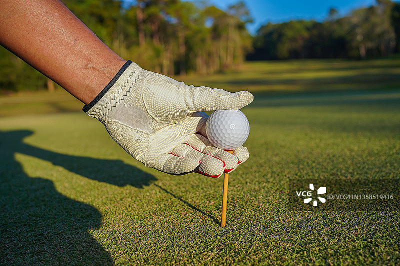 手高尔夫球手将球放在草地上开球。在球场上手持高尔夫球与球座，特写图片素材