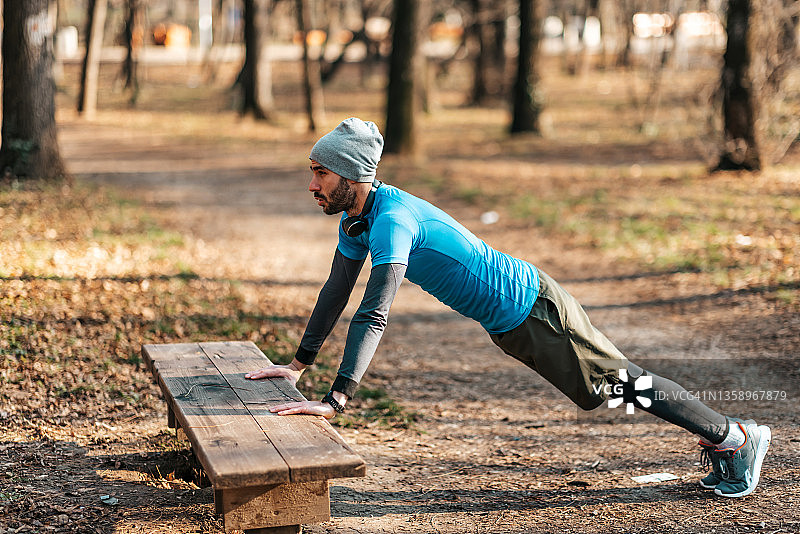 年轻人锻炼使用一个木制的公园长凳提高自己的手臂，以增强他的肌肉，在健康的生活方式的概念与拷贝空间的侧面图片素材