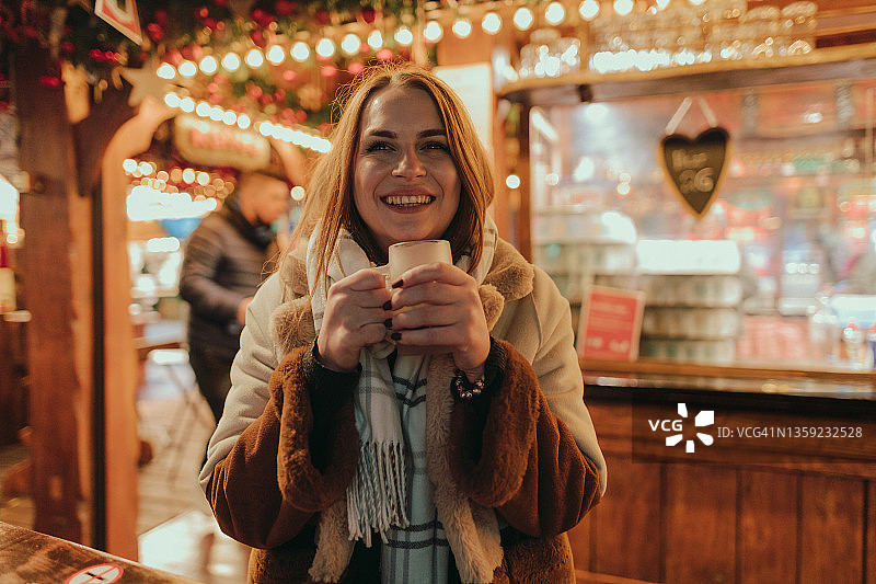 微笑的女人在圣诞市场享受一杯热葡萄酒图片素材