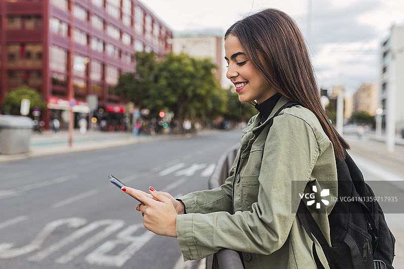 背着背包在城市里使用手机的微笑女人图片素材