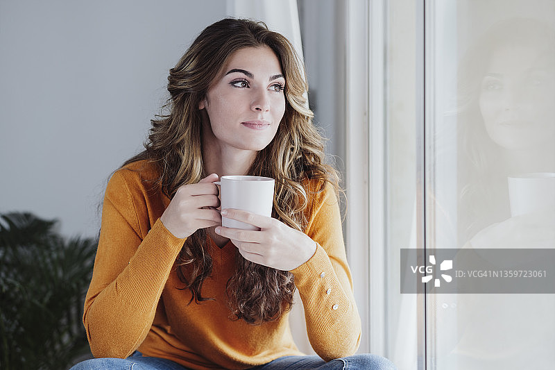 年轻女子拿着咖啡杯在窗口在家里图片素材