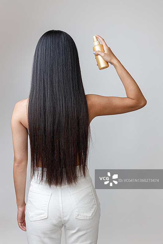 黑发年轻女子在头发上喷洒修护血清图片素材