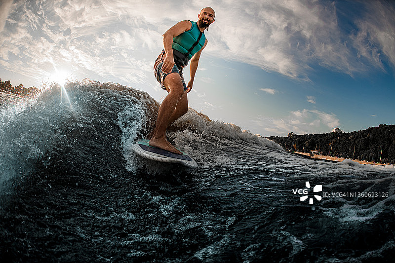快乐的活跃的男子醒来冲浪板在蓝色的水在夏天的一天图片素材