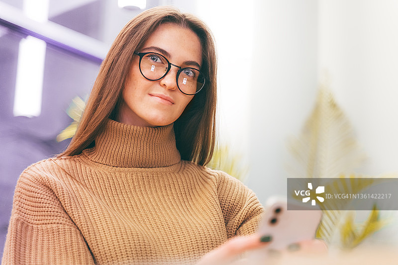 年轻时尚的女商人戴着智能眼镜，正在用手机发短信，看着镜头微笑图片素材