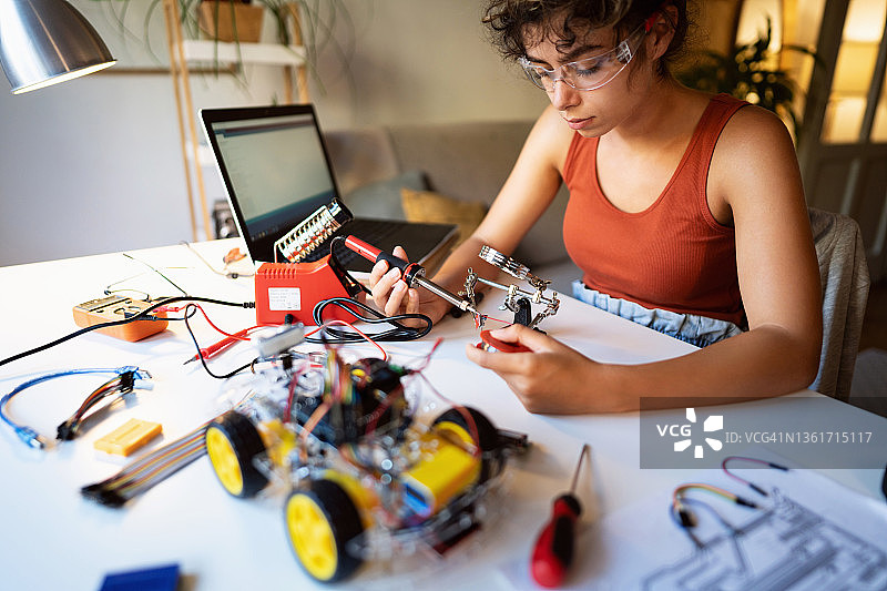 工程系女学生，在制造机器人汽车时，用烙铁焊接建筑零件的金属丝图片素材
