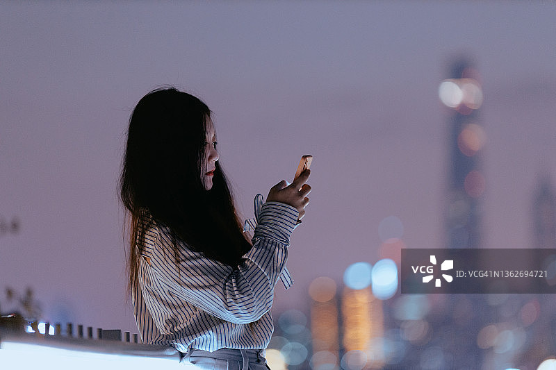 中国上海，一名年轻的亚洲女性在夜晚使用智能手机图片素材
