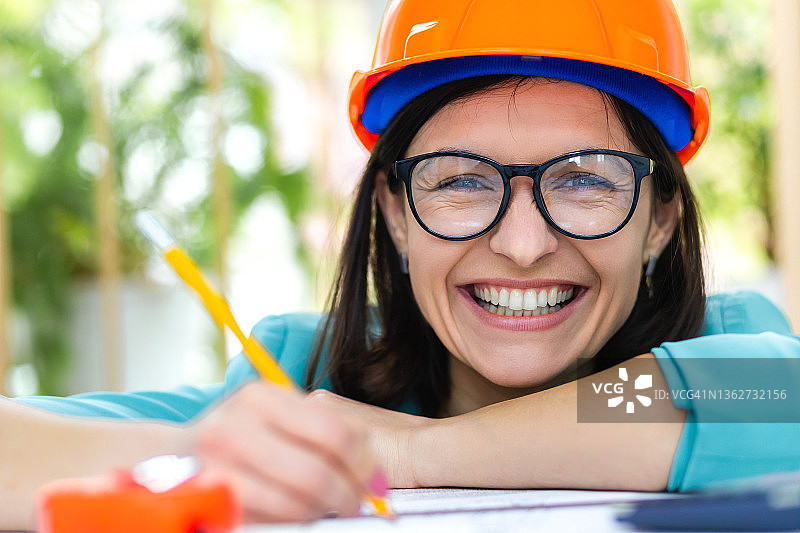 微笑的女工程师戴着橙色头盔的照片。图片素材