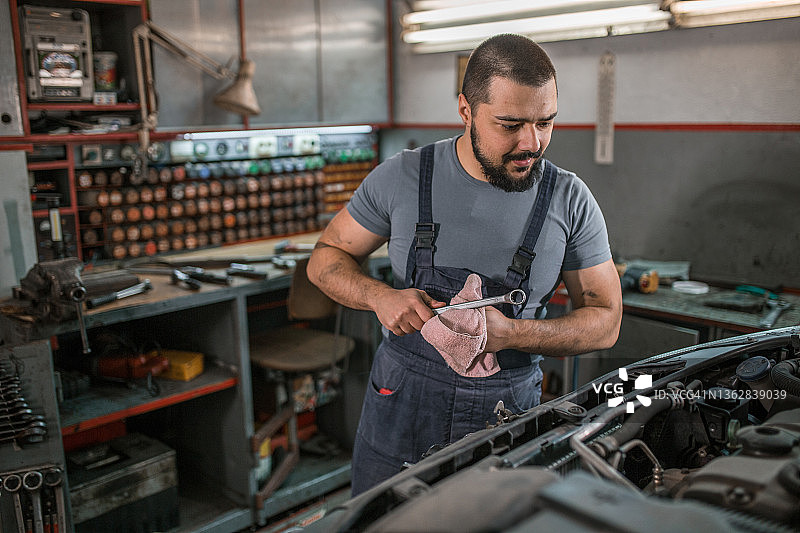 微笑的汽车修理工在汽车修理厂检查汽车发动机图片素材