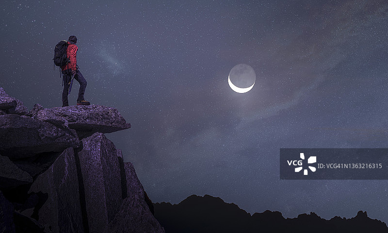 一个登山者站在岩石上看月亮图片素材