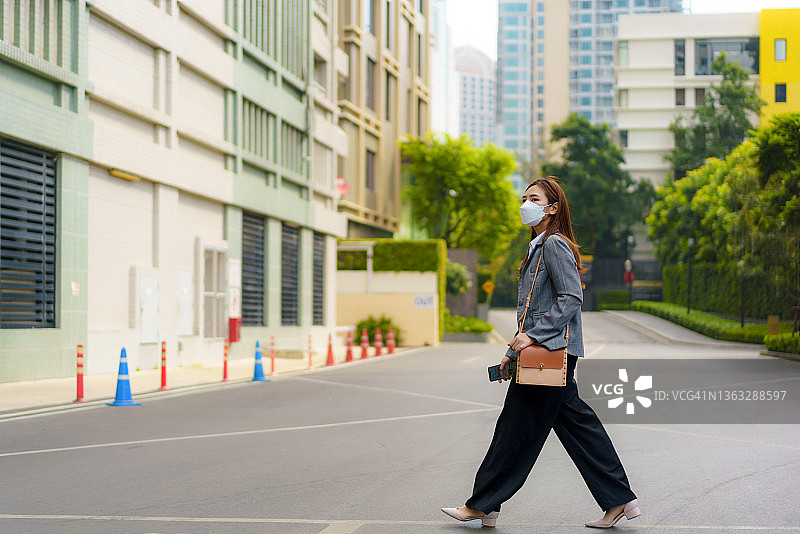 全长年轻的亚洲办公室妇女带着面具走在斑马线上去工作在城市的早上图片素材