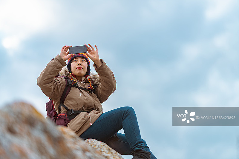年轻的女徒步旅行者坐在山上的岩石下阴天冬天图片素材