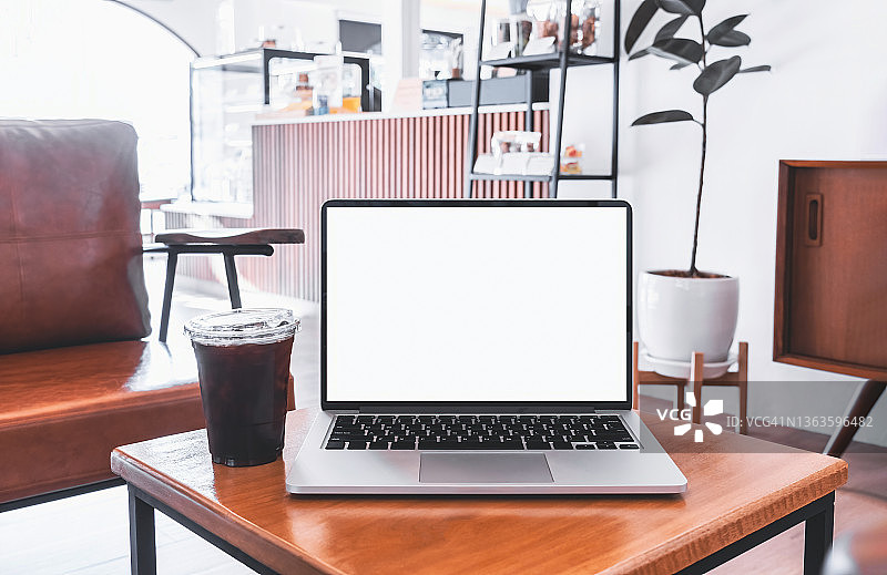 笔记本电脑空白屏幕上的桌子在咖啡馆的背景。笔记本电脑与空白屏幕的桌子上的咖啡店模糊的背景。图片素材