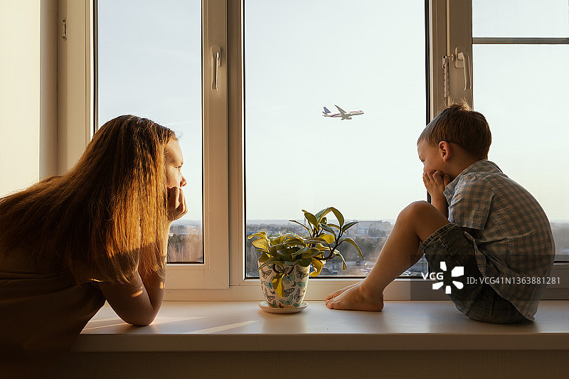 悲伤的孩子们望着天空中飞行的飞机，等待隔离结束。儿童抑郁症概念在家庭生活中的流行图片素材