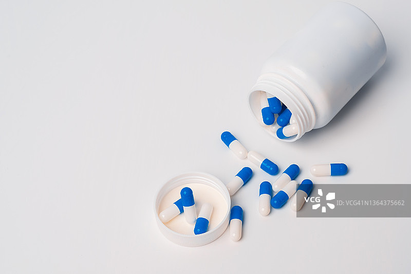 蓝白色药丸从药瓶中溢出，白色的背景。一瓶蓝白药丸。医学。药物治疗图片素材