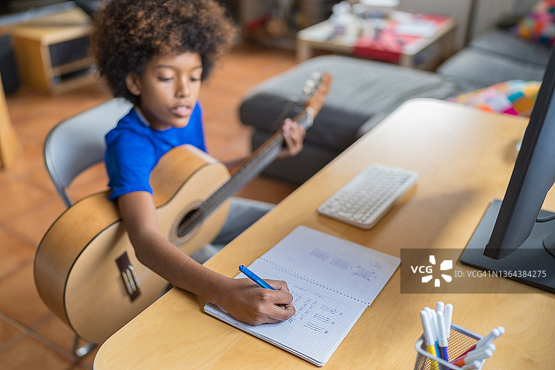 非裔美国男孩在网上吉他课上记笔记。图片素材